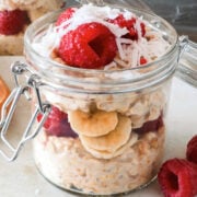small jar of overnight oats topped with coconut, raspberry and banana slices