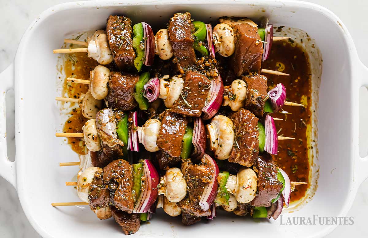 a baking dish with marinated beef kabobs