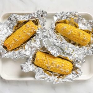 overhead view of 3 pieces of corn on the cob on top of foil topped with a garlic butter sauce.