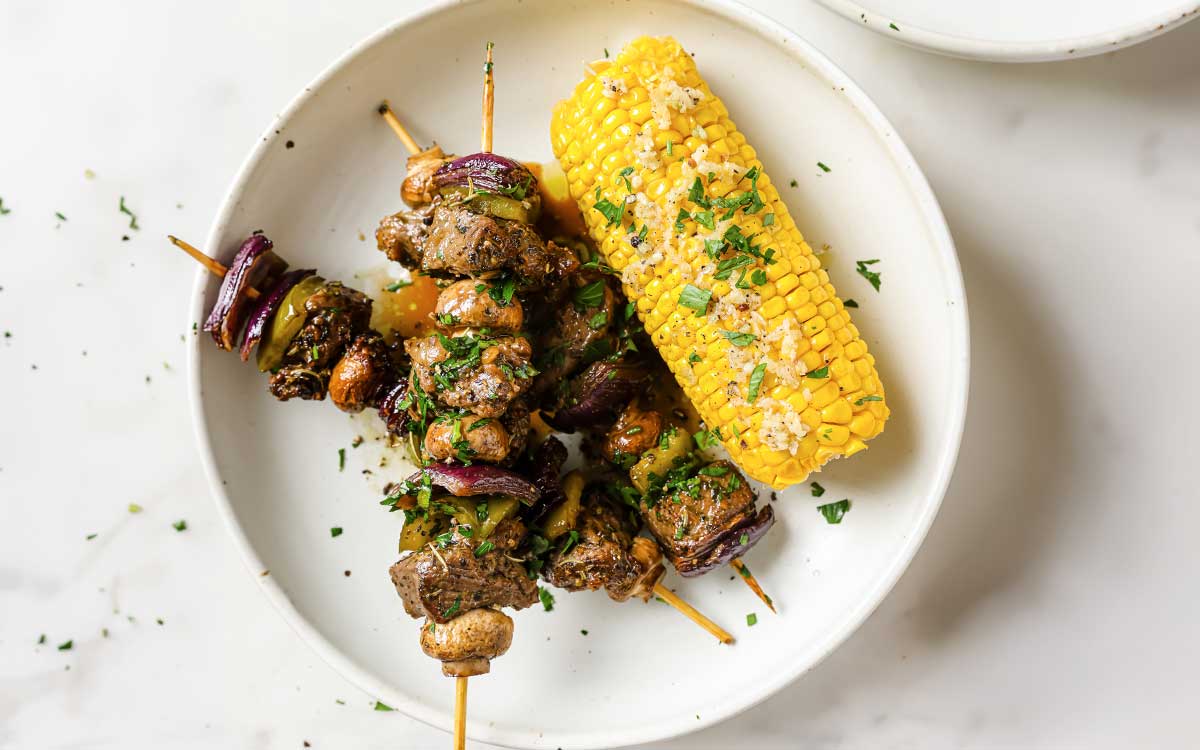 a plate with beef kabobs and oven baked corn on the cob.