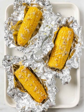 overhead view of 3 pieces of corn on the cob on top of foil topped with a garlic butter sauce.