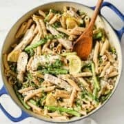 overhead view of lemon garlic chicken pasta in a pan topped with a lemon slice and a wooden serving spoon on the side