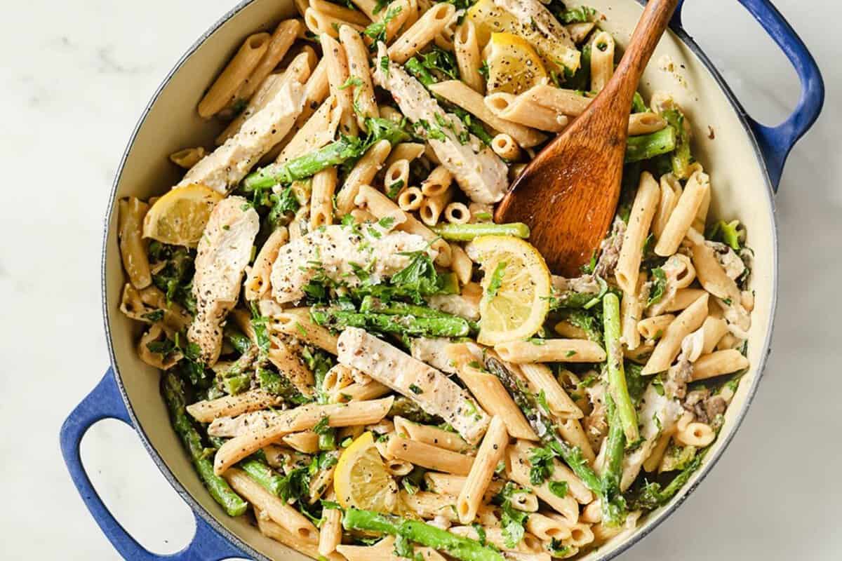 overhead view of lemon garlic chicken pasta in a pan topped with a lemon slice and a wooden serving spoon on the side