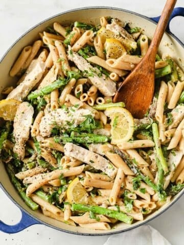 overhead view of lemon garlic chicken pasta in a pan topped with a lemon slice and a wooden serving spoon on the side