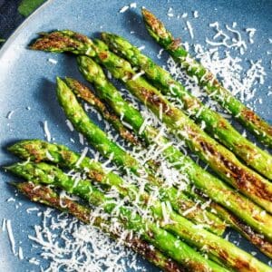 Roasted asparagus spears on a blue plate, topped with Parmesan cheese