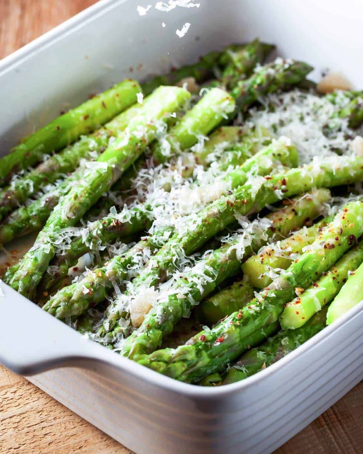 Roasted asparagus spears in a baking dish, topped with Parmesan cheese