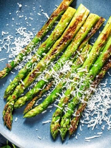 Roasted asparagus spears on a blue plate, topped with Parmesan cheese