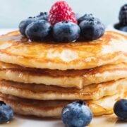 stack of pancakes made with greek yogurt on a plate with blueberries and raspberries