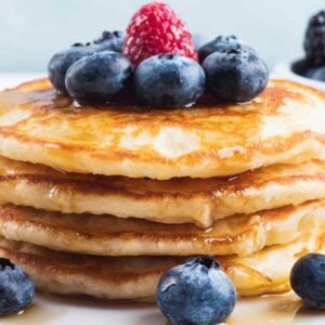 stack of pancakes made with greek yogurt on a plate with blueberries and raspberries