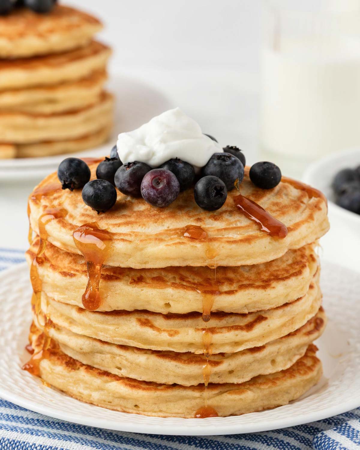 large stack of greek yogurt pancakes topped with blueberries, yogurt and syrup