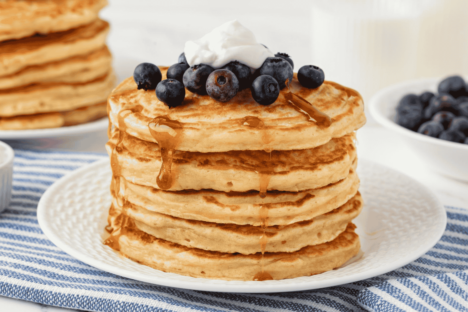 large stack of greek yogurt pancakes topped with blueberries, yogurt and syrup