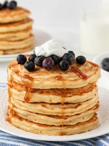 large stack of greek yogurt pancakes topped with blueberries, yogurt and syrup