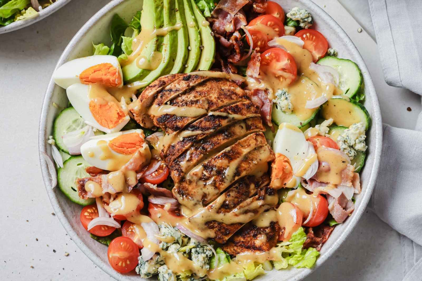 a large salad bowl with cobb chicken salad with avocado, hard-boiled eggs, tomatoes, cucumber, lettuce, and onions