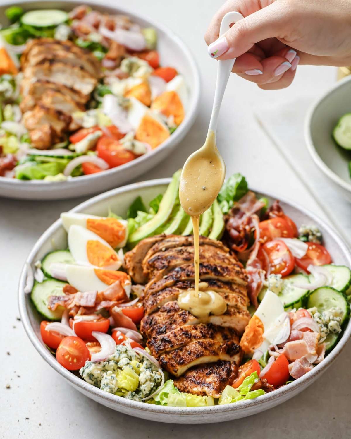a hand drizzling dressing over a large bowl of Cobb chicken salad