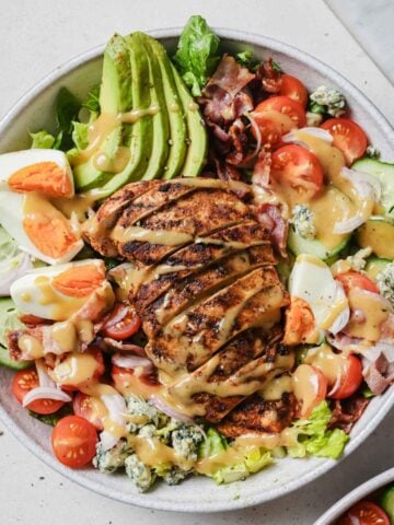 a large salad bowl with cobb chicken salad with avocado, hard-boiled eggs, tomatoes, cucumber, lettuce, and onions