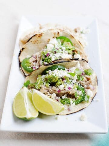 slow cooker tequila lime pulled pork tacos and lime wedges on the side