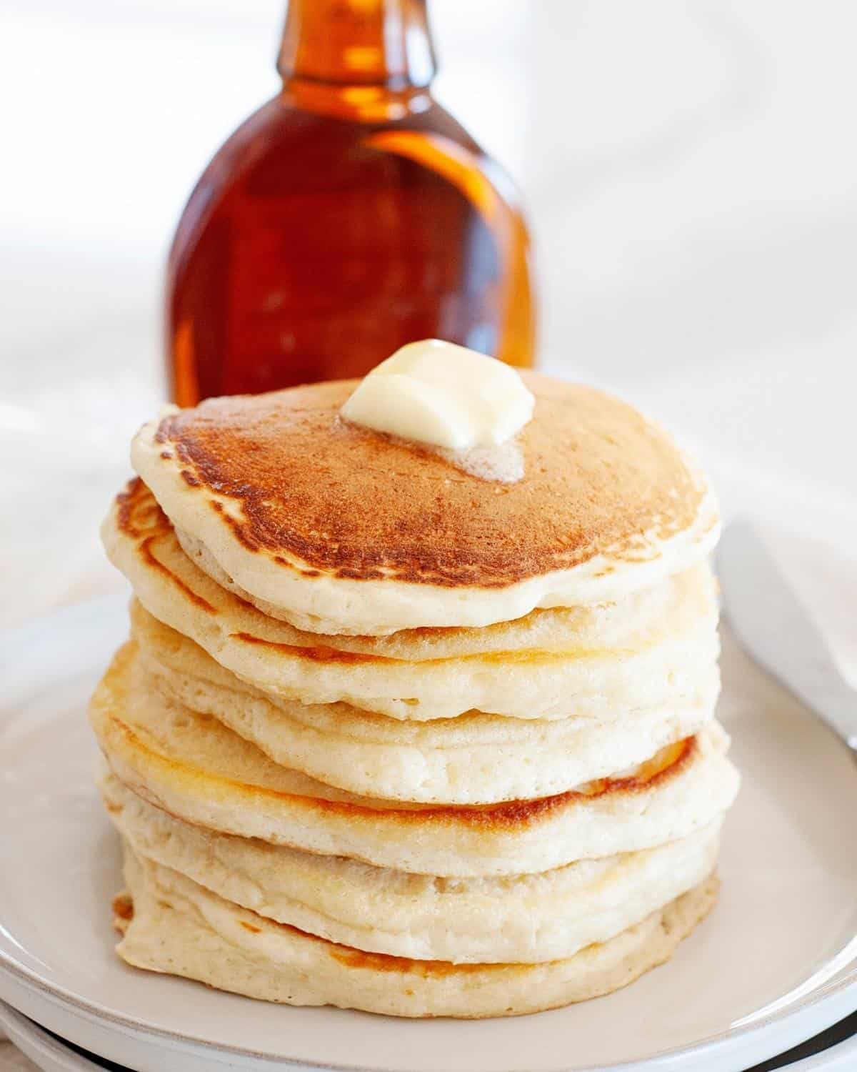 Pancakes without eggs on a plate topped with syrup and butter with a syrup bottle in the back
