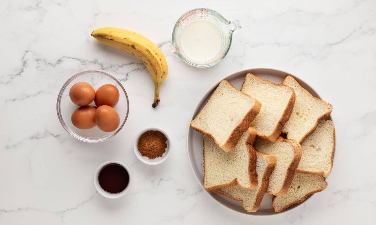 banana, eggs, milk, vanilla, and cinnamon in bowls, plus a plate with slices of bread