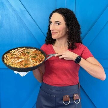 Laura Fuentes standing in front of a blue door holding a skillet of dinner