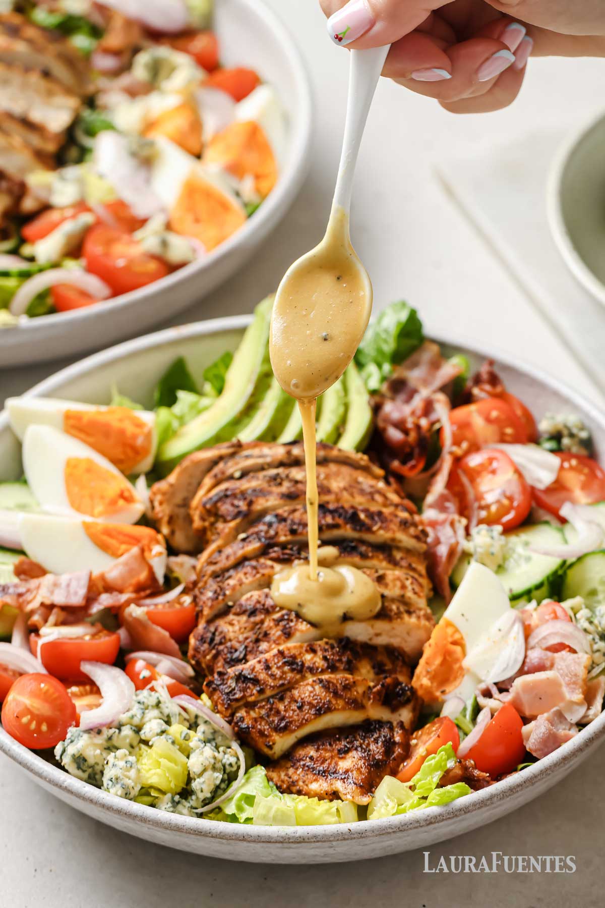 a person drizzling dressing over a cobb salad