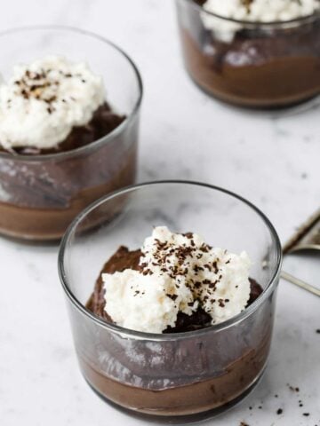 three small bowls with chocolate avocado mousse topped with whipped cream