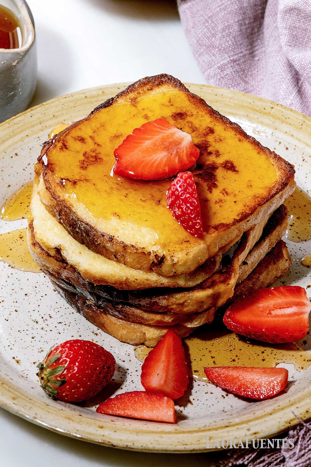 stack of French toast topped with syrup and strawberries