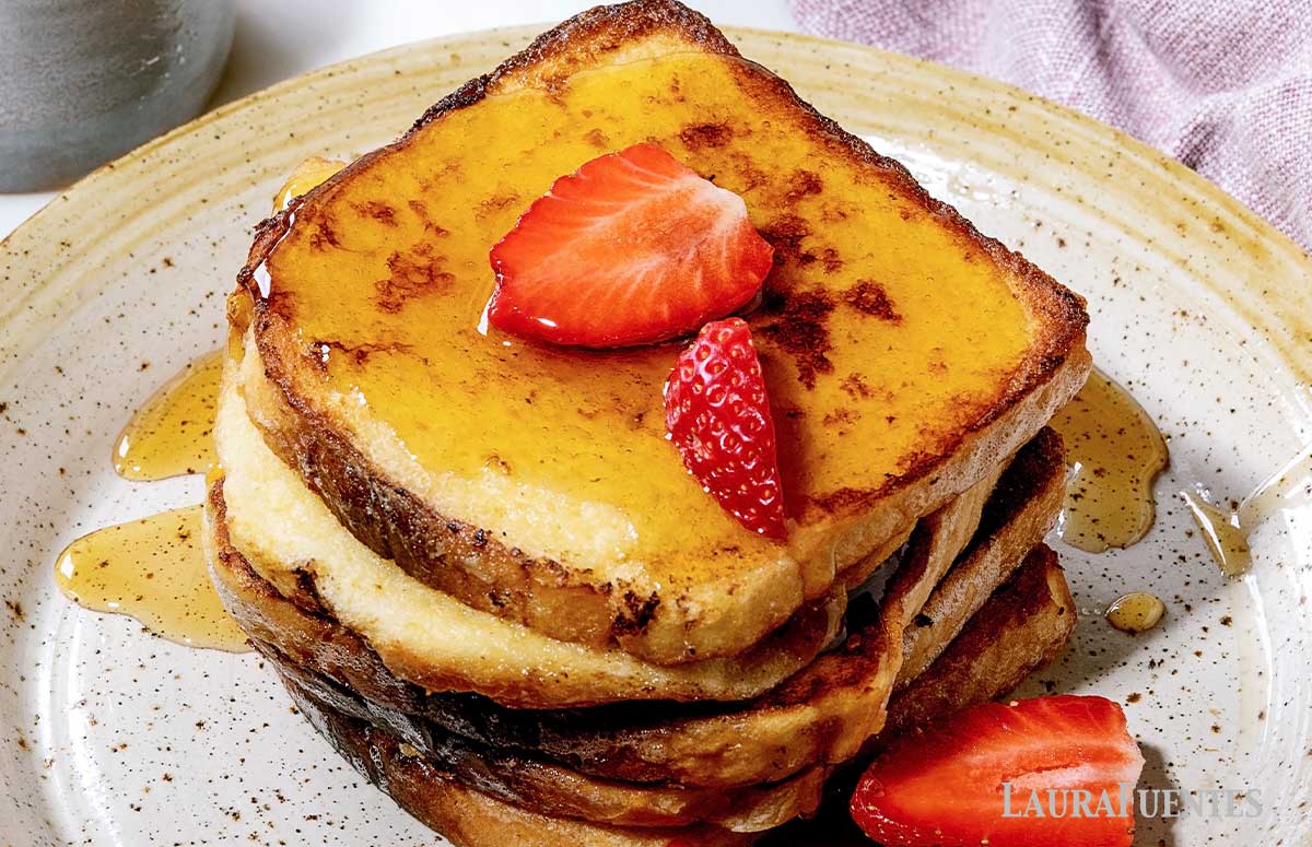 large stack of french toast topped with syrup and sliced strawberries