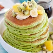 closeup of large stack of green pancakes with diced fruit on top