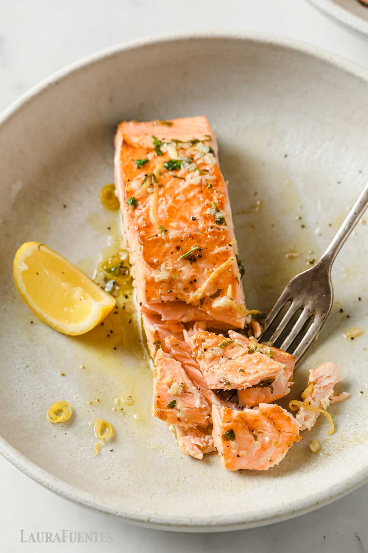 a dish with salmon fillet, a fork, and a lemon wedge