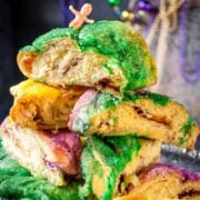 stack of king cake slices topped with colorful mardi gras sugars and a small plastic baby