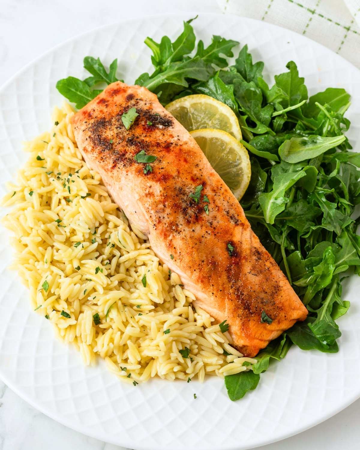 overhead view of baked frozen salmon on a plate served with some yellow rice and salad greens with lemon slices