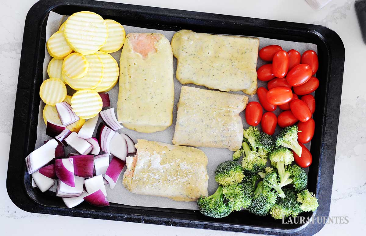 overhead view of a sheet pan with four frozen salmon fillets and chopped vegetables