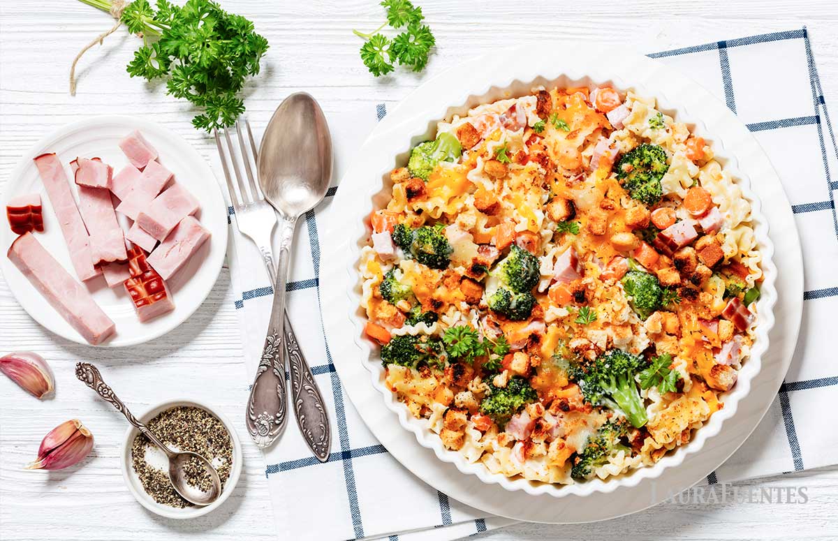 overhead view of macaroni and cheese with broccoli toppings and sliced ham on the side in a white plate