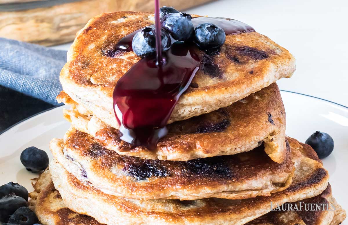 large stack of blueberry pancakes with a drizzle of blueberry syrup