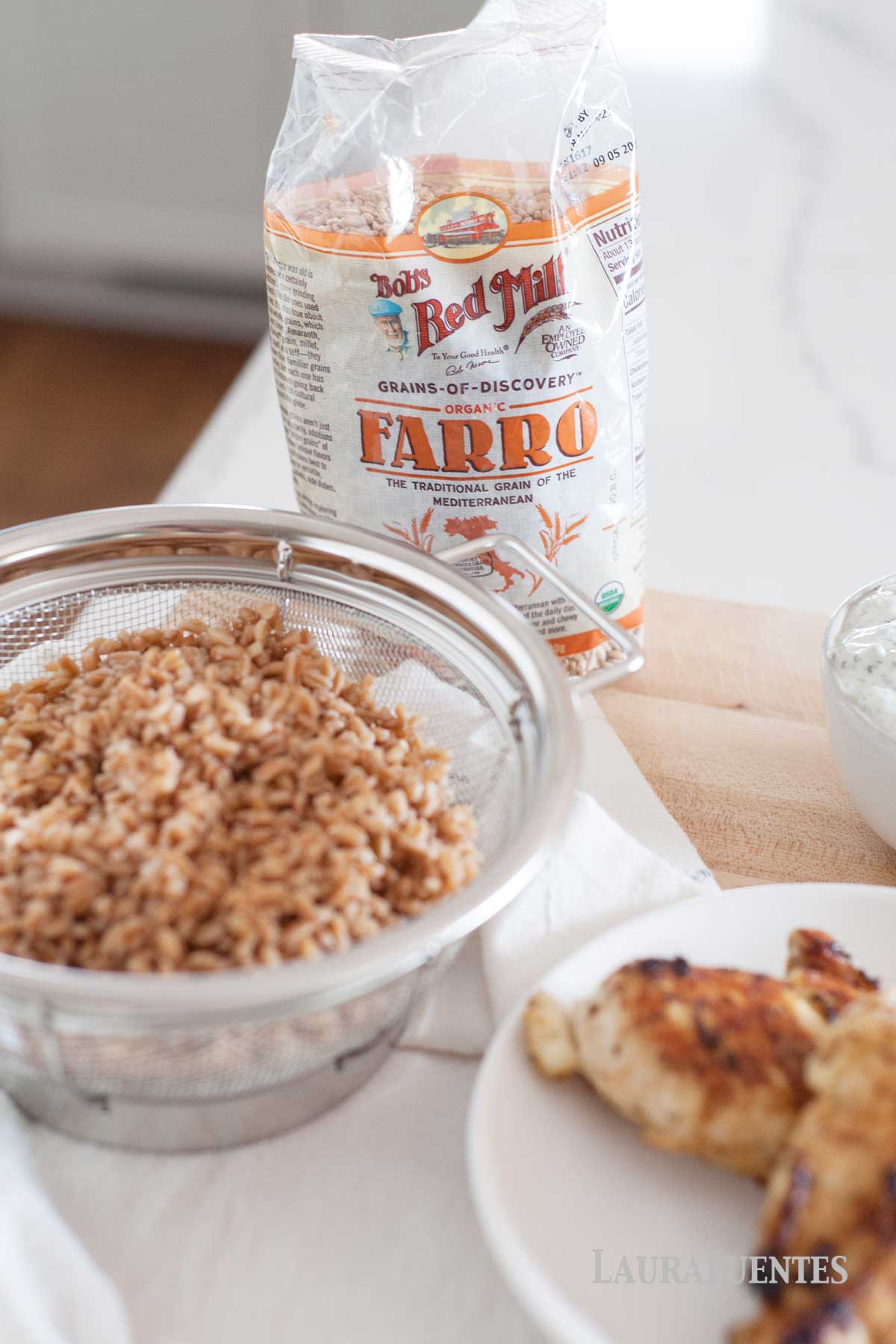 cooked farro in a colander, a pack of farro, and chicken on a plate