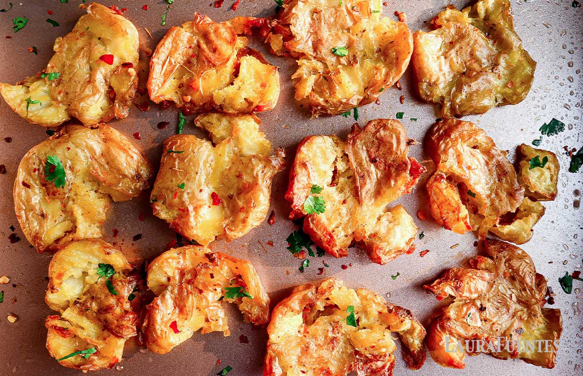 twelve smashed potatoes on a sheet with herb topping