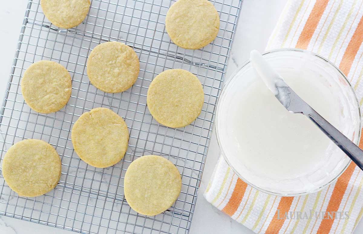 sugar cookies on a cooling rack with a bowl of icing