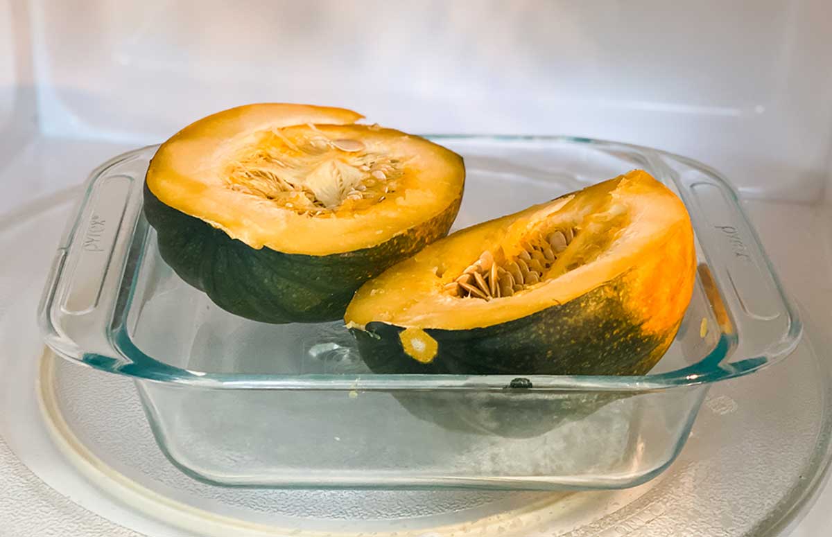 two acorn squash halves in a baking dish in the microwave