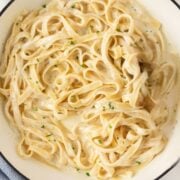 overhead view of a large skillet with homemade alfredo sauce mixed with cooked fettuccine pasta