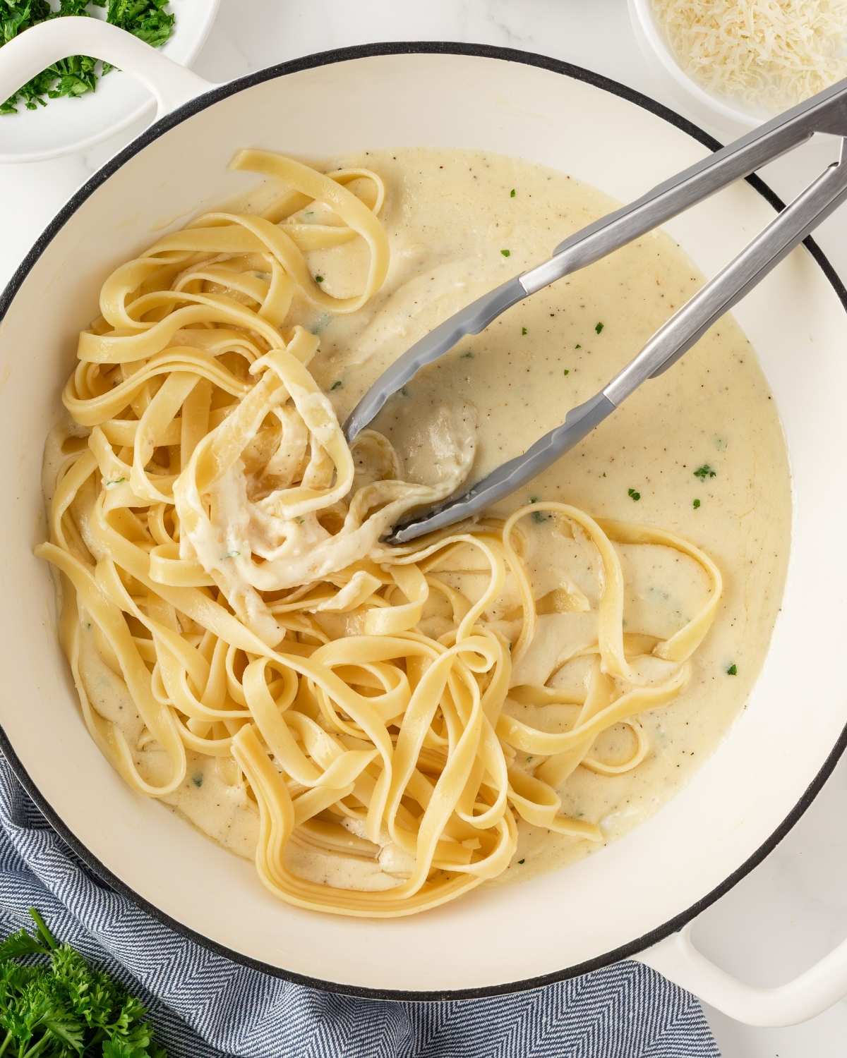 overhead view of a large skillet with homemade alfredo sauce being mixed with cooked fettuccine pasta