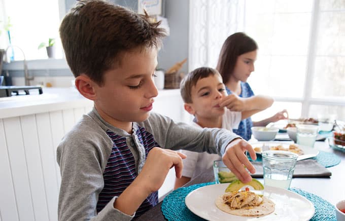 three kids eating tacos at a dining room table