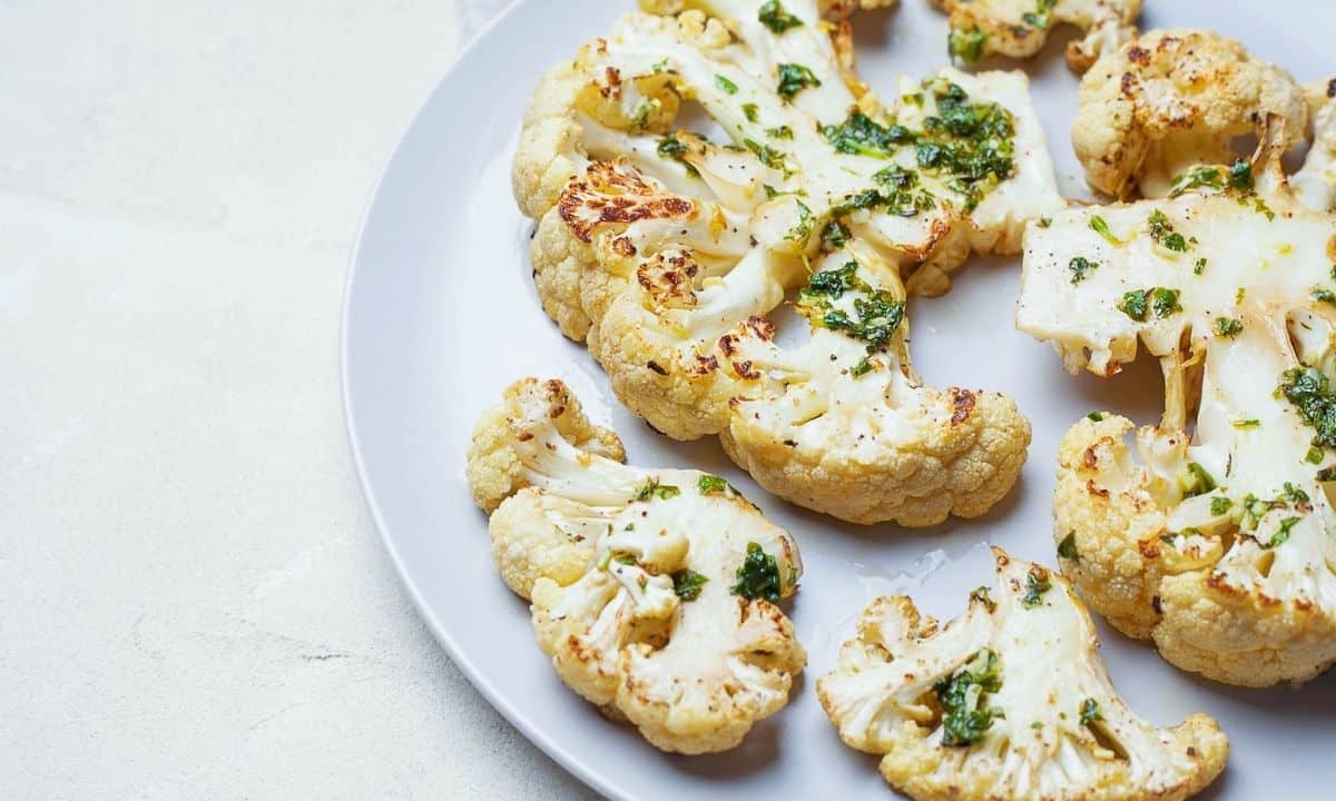 a white dish with roasted cauliflower sticks