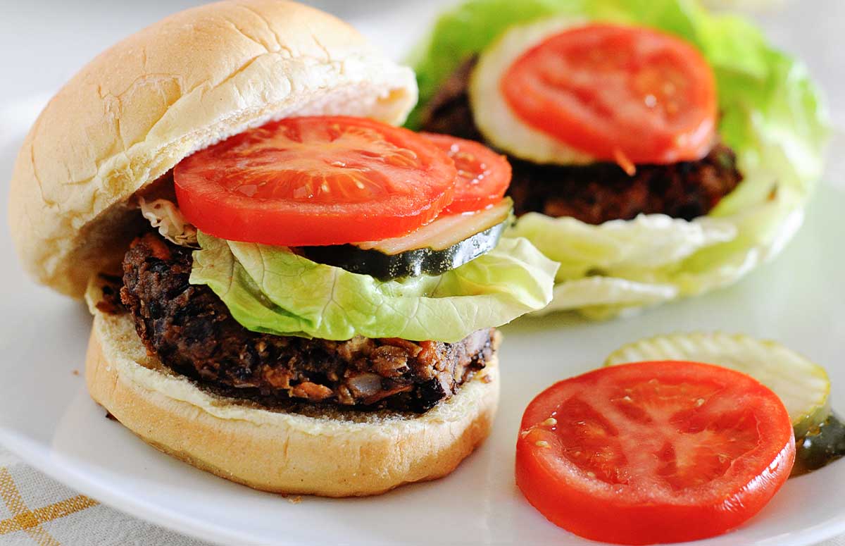 two black bean burgers on a plate with tomatoes and lettuce