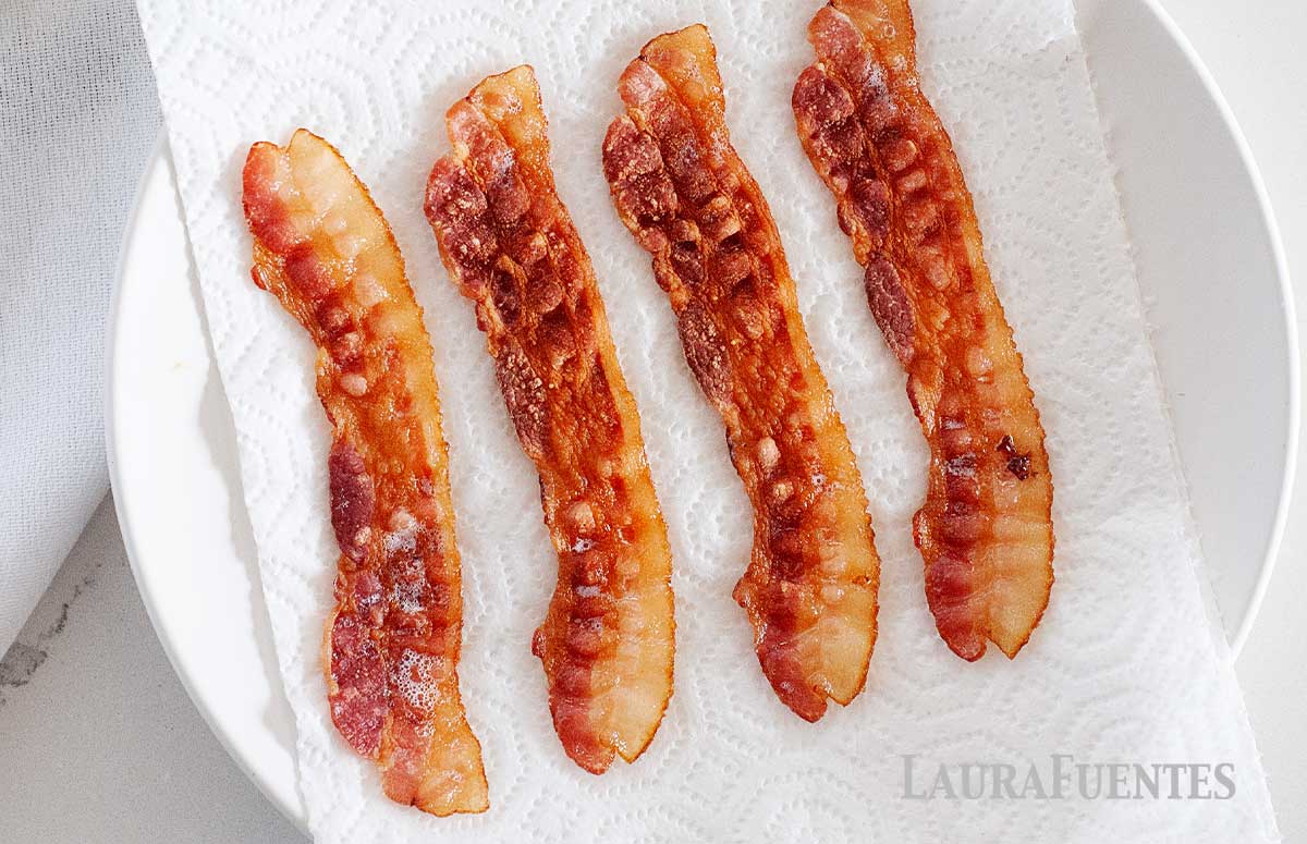 four crispy slices of bacon on a plate with paper towels