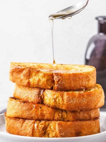 stack of four French toast slices with syrup being drizzled over the top from a spoon