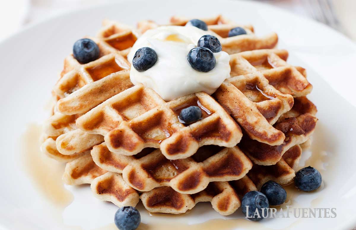 three waffles stacked on a plate topped with whipped cream and blueberries