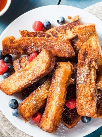 pile of French toast sticks on a plate with fresh berries