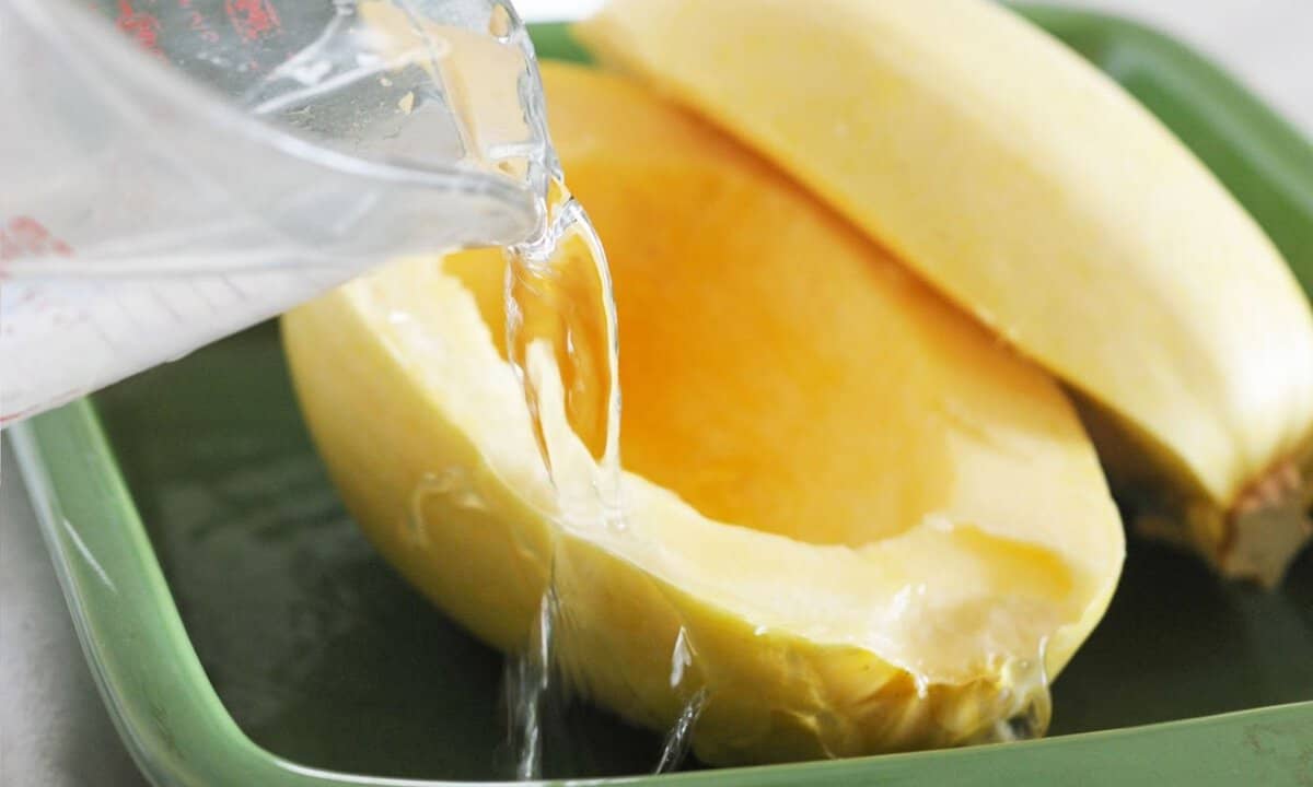 water being poured in a baking dish with raw spaghetti squash