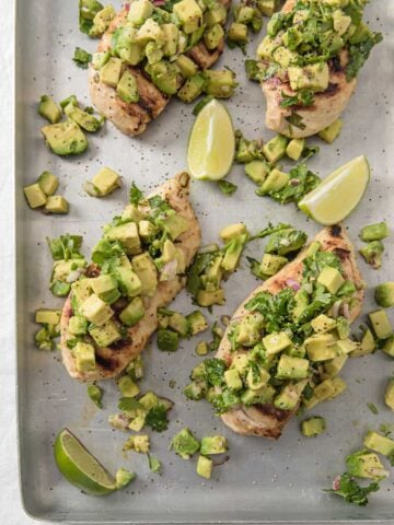 baked chicken breasts topped with avocado salsa on a baking sheet