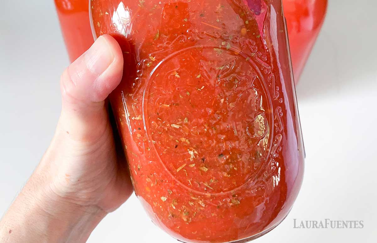 a hand holding a slow cooker tomato sauce jar
